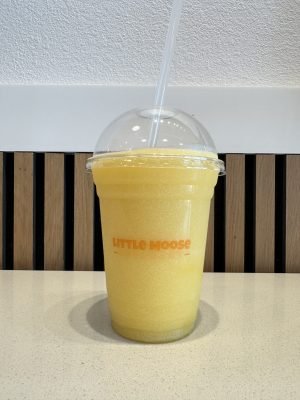 An icy, bright yellow mango slush in a clear cup featuring the Little Moose Creamery logo, served with a dome lid and a clear straw.